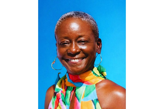 Portrait of Rena Brodhurst smiling, wearing colorful attire against a blue background