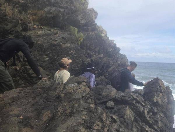A group of people hiking a rocky mountain trail in front of the Caribbean Sea. 